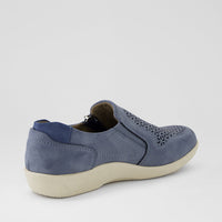 A single slip-on shoe in dusty blue suede with laser-cut geometric patterns on the toe, shown from a three-quarters rear angle against a light gray background.