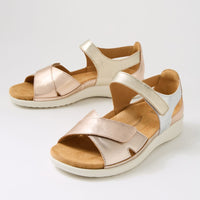 Pair of rose gold sandals with beige soles on a light gray background