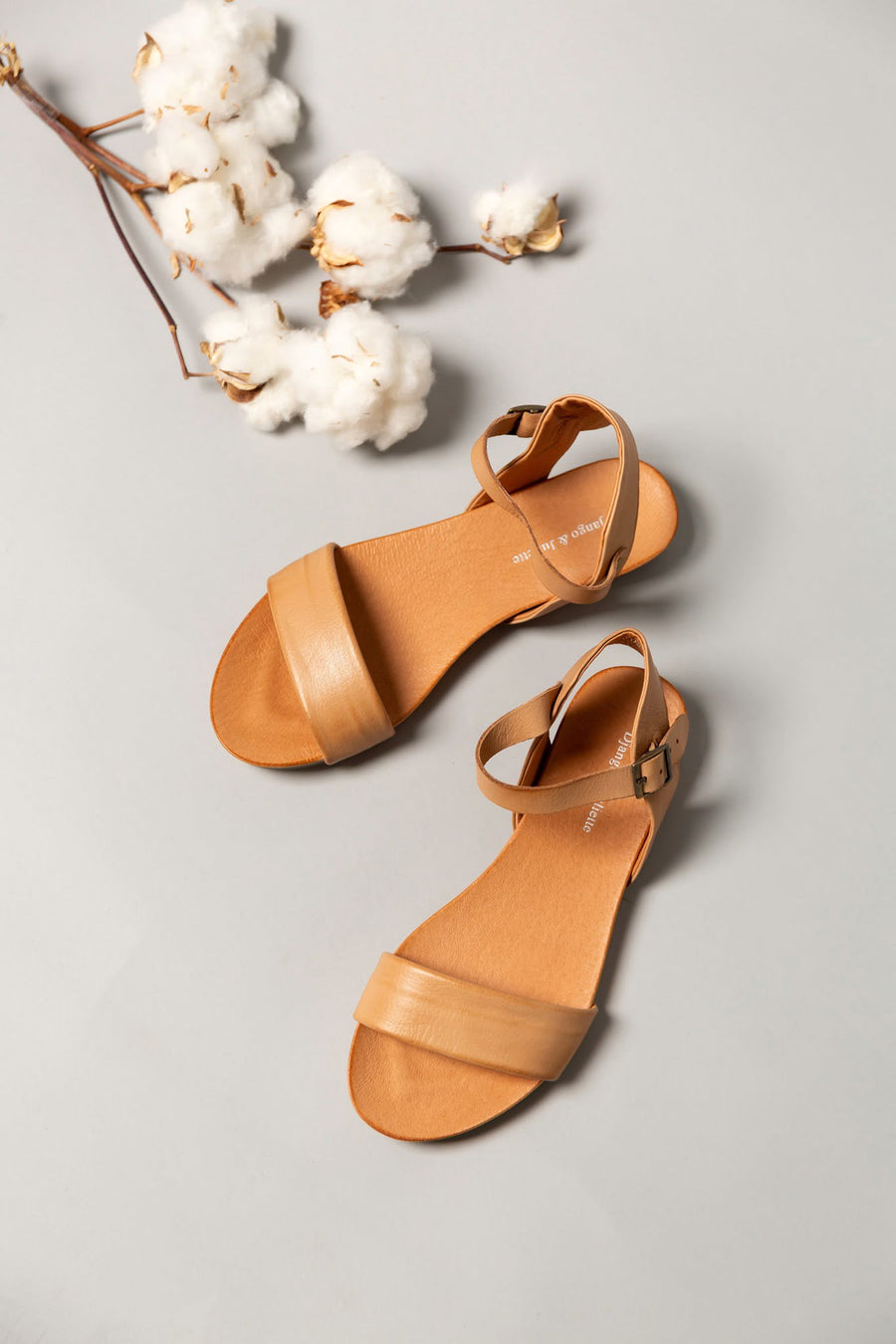 Beautiful, tan Django & Juliette sandals resting on a grey table, with white flowers beside them.