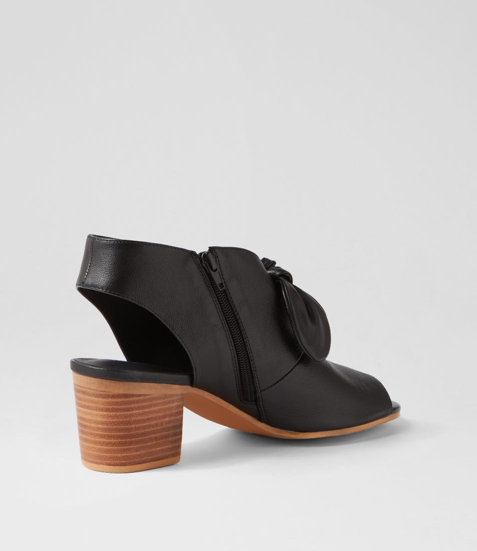 Black heeled shoe with a wooden sole on a light gray background