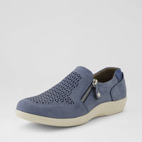 A single slip-on shoe in slate blue suede with geometric laser-cut perforations on the toe, a silver zipper, and a thick cream-colored sole, shown against a light gray background.