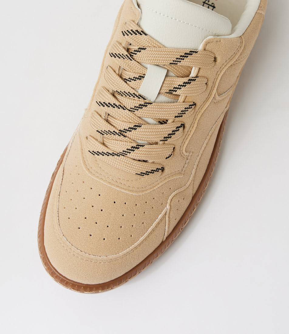 A close-up of a beige suede sneaker with black-and-white patterned laces, a white tongue label, and a brown gum sole, photographed on a light gray background.