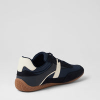A low-top athletic sneaker shown from a rear three-quarter angle, featuring navy blue and off-white panels with a brown gum sole, set against a light gray studio background.