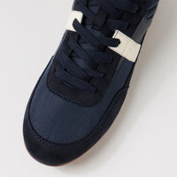 Close-up of a navy blue low-top sneaker with matching navy laces and a contrasting off-white horizontal stripe near the lace area, photographed on a clean light gray background.