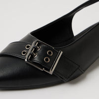 A close-up of a black leather slingback flat shoe featuring a decorative strap across the toe with metal eyelets and a silver-tone buckle.