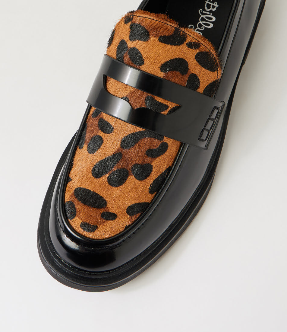 A close-up of a loafers shoe featuring a brown and black leopard print hair-on-hide upper with a glossy black leather strap and sole.