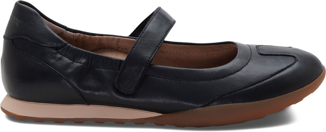 A black leather Mary Jane flat shoe with a hook-and-loop strap, brown insole, and brown outsole, shown from a side angle on a white background.