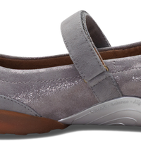 A single women's Mary Jane shoe in metallic silver-gray suede and synthetic fabric, featuring a hook-and-loop strap, a sculpted white midsole, and a brown outsole, shown from a side profile on a white background.