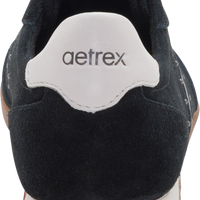 Close-up rear view of a black suede sneaker with a white heel tab featuring the 'aetrex' logo, set against a plain white background.