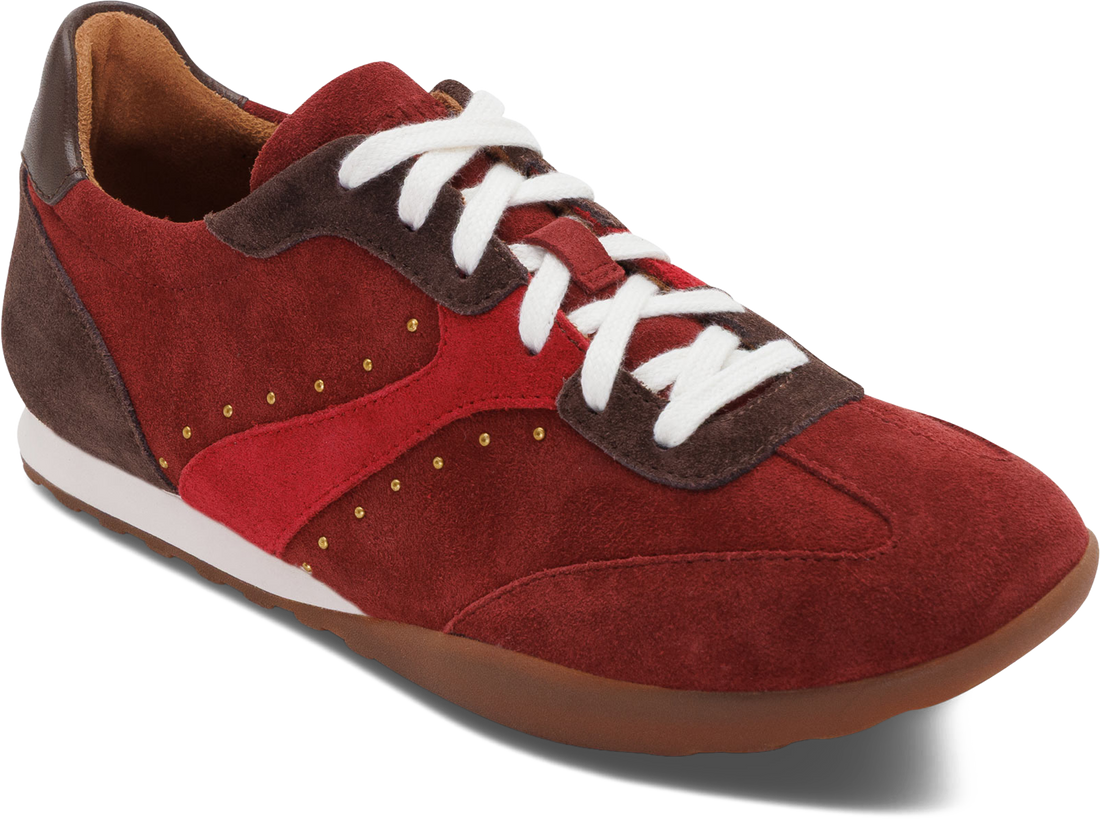 A low-top sneaker in red suede and fabric with dark brown suede overlays, white laces, and gold-tone decorative studs, shown on a white background.