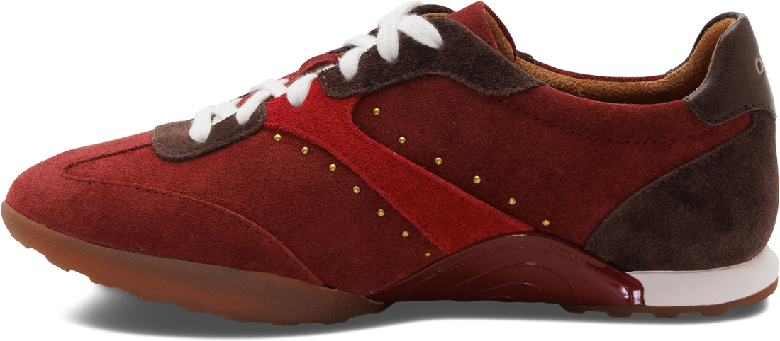 A red suede and leather sneaker with white laces, brown heel tab, and gold-tone decorative studs, shown from a side profile on a white background.