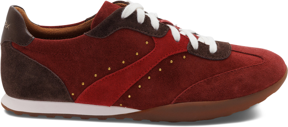 A red suede and leather sneaker with white laces, a white midsole stripe, brown heel and toe accents, and small gold stud details, shown from a side profile on a white background.